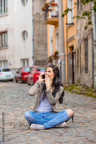 Girl with cellphone sitting in a middle of a street.