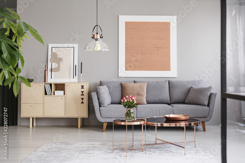 Large painting on a gray wall above an elegant sofa with cushions in a stylish living room interior with copper furniture © Photographee.eu