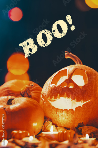 Real photo with text of happy carved pumpkin placed on the ground with leaves and candles