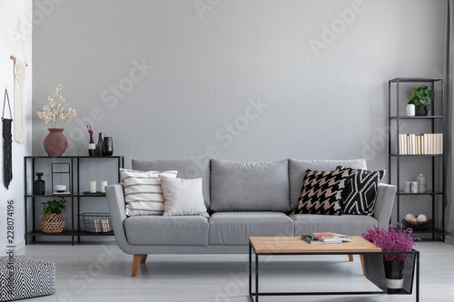 Metal black shelves with books, candles and plants behind the grey sofa with patterned pillows, real photo with copy space on the wall