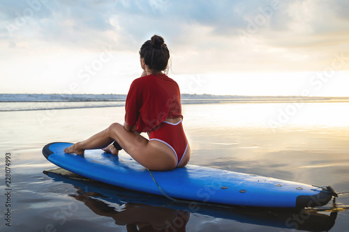 Woman sitting on surfboard on the beach after her surfing session © blackday
