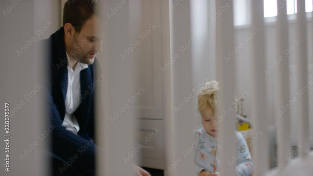 Young father and son playing together, shot through a baby's cot bars