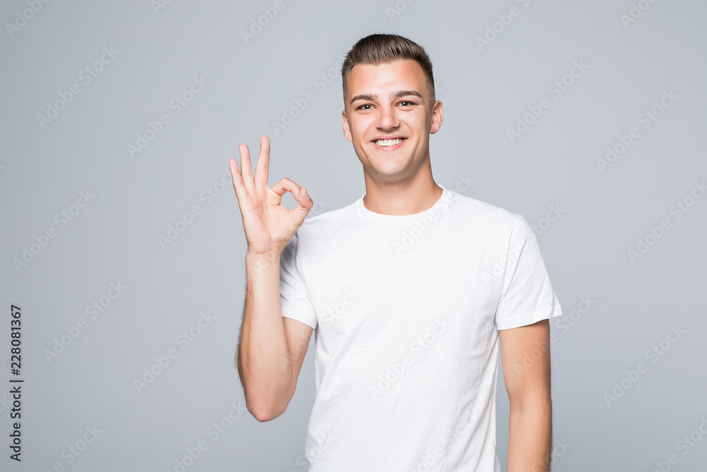 Portrait of a cheerful young man showing okay gesture on the gray background Portrait of a cheerful young man showing okay gesture on the gray background