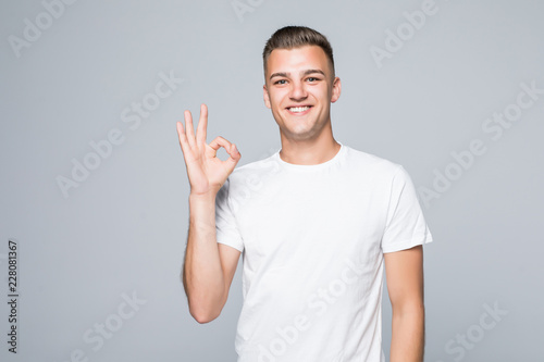 Portrait of a cheerful young man showing okay gesture on the gray background © dianagrytsku