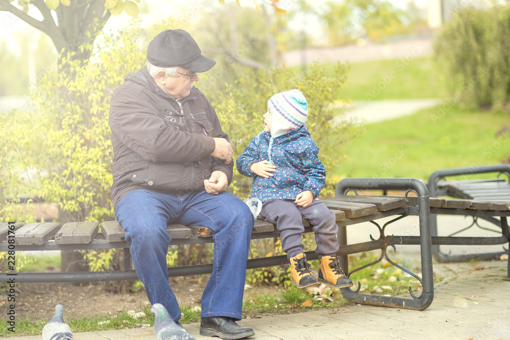 Fototapeta premium old grandfather and little grandson are sitting on a bench. concept of generations family. walk together