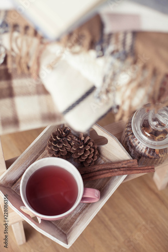 Plaids. A cup of hot tea. Autumn cozy interior. On a wooden chair is a stack of warm blankets. Candles  leaves  cones  basket  cinnamon. Book and glasses. Autumn. Winter.