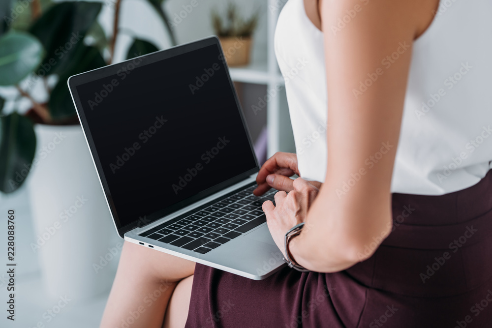 Naklejka premium cropped view of businesswoman using laptop with blank screen