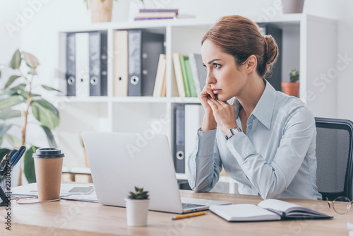 thoughtful adult businesswoman sitting at workplace and looking away