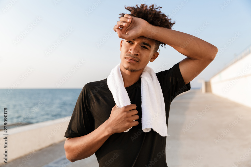 Handsome young guy sportsman standing with towel outdoors on the beach. Handsome young guy sportsman standing with towel outdoors on the beach.