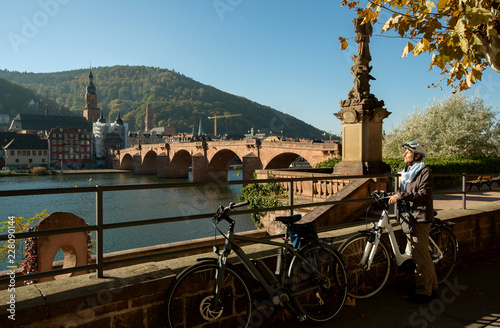 Fahrradfahrerin genießt die Herbstsonne , Blick auf Heidelberg, Altstadt mit Nepomuk Figur und Alter Brücke