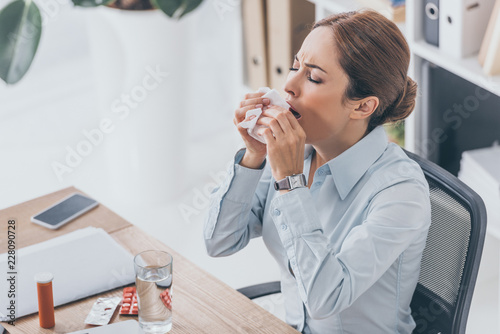 high angle view of diseased adult businesswoman sneezing at workplace photo