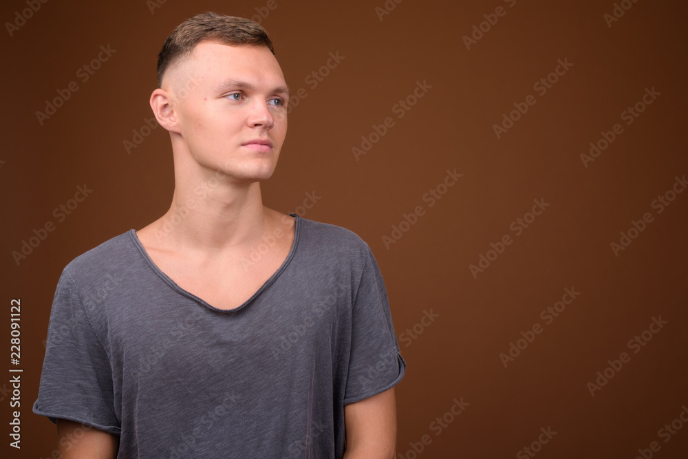 Young man wearing gray shirt against brown background Young man wearing gray shirt against brown background