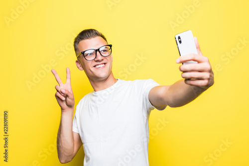 Obraz na płótnie Cheerful man looking at camera and taking selfie on yellow background