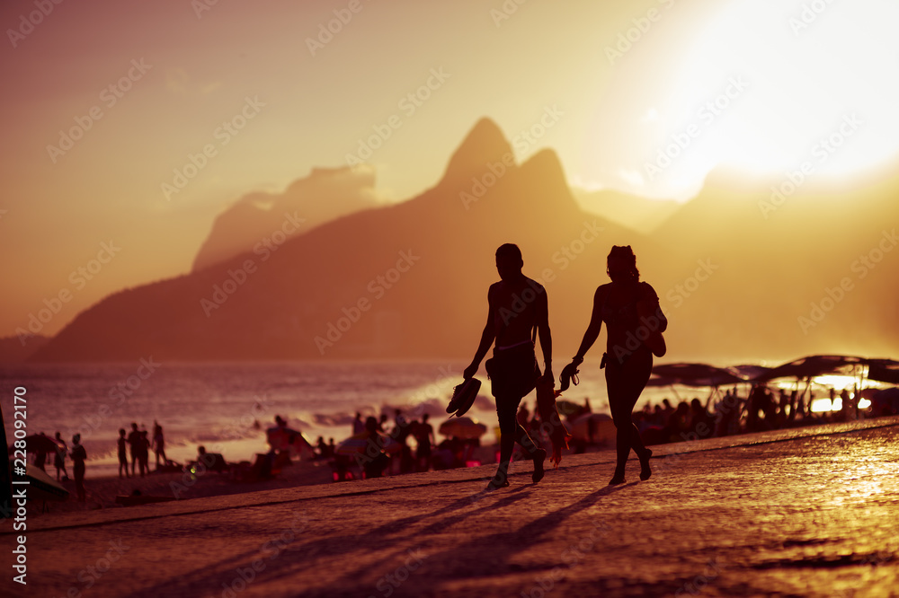 Scenic golden sunset view of Ipanema Beach with shadow silhouettes walking on the Arpoador boardwalk in Rio de Janeiro, Brazil