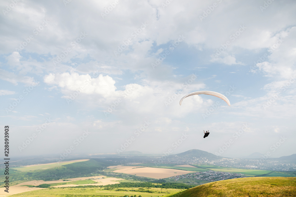 A white-orange paraglider flies over the mountainous terrain A white-orange paraglider flies over the mountainous terrain