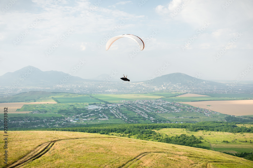 A white-orange paraglider flies over the mountainous terrain A white-orange paraglider flies over the mountainous terrain