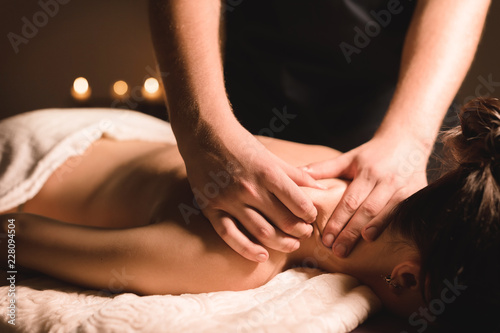 Male manual worker doing spa massage of shoulders and neck to young girl in dark room