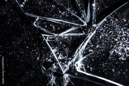 A broken glass on a dark surface, showing extreme damage, with many sharp shards. Macro close-up shot. Useful texture overlay.
