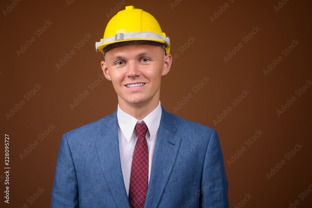 Young businessman wearing hardhat against brown background Young businessman wearing hardhat against brown background