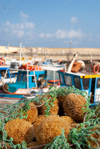 Focus on a net full of natural sea sponges by a harbour in Crete, with blurred boats in background