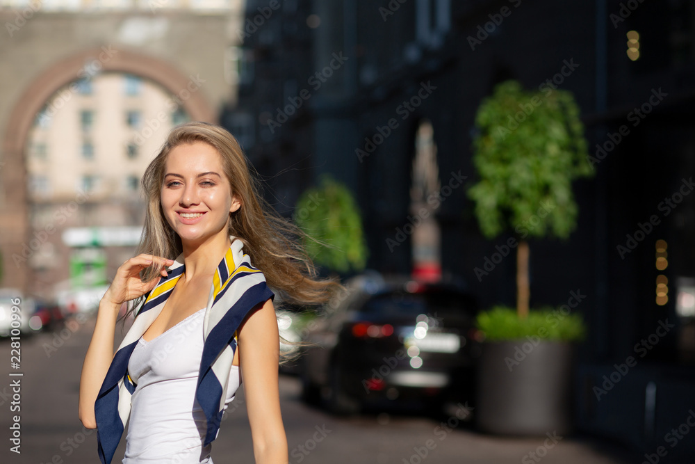 Positive blonde model with long curly hair wearing shawl and white shirt posing with sun light