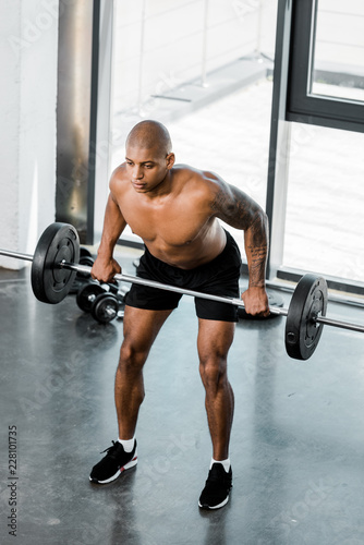 high angle view of muscular bare-chested african american sportsman lifting barbell in gym