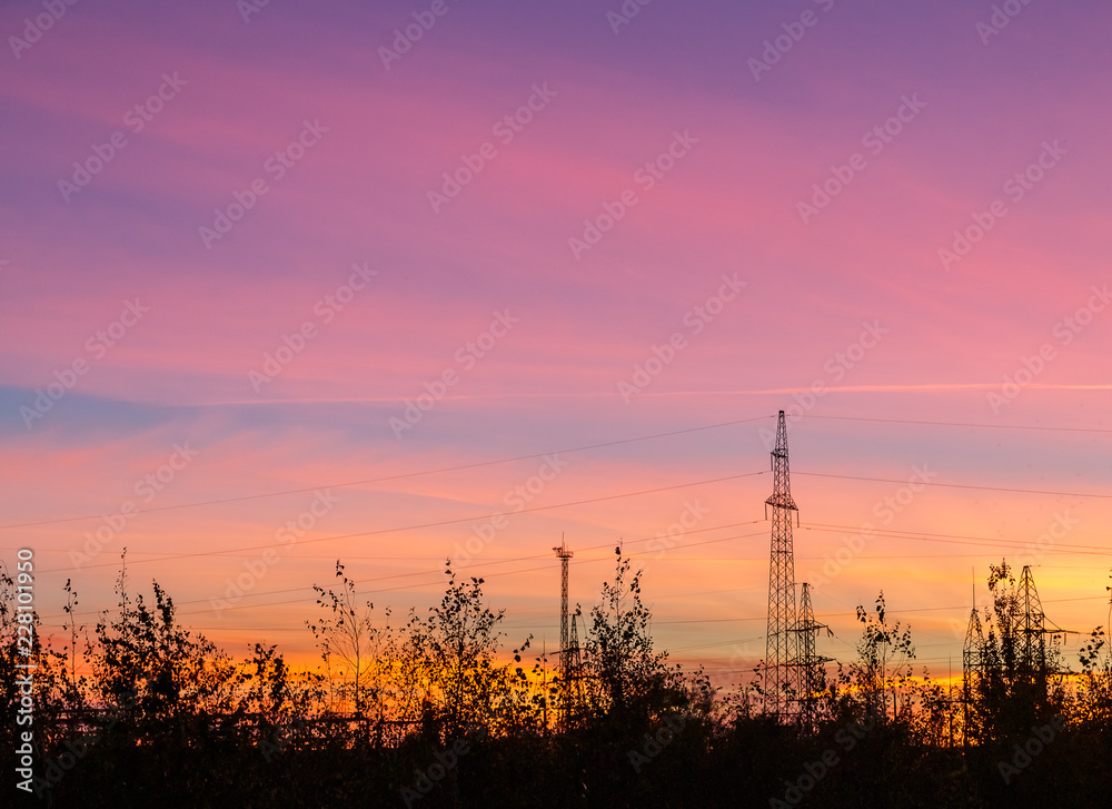 Bright colorful sunset over power line and trees.