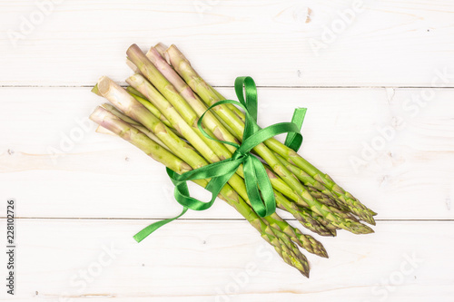 Bundle of lot of whole fresh green asparagus spear tied by green ribbon flatlay on white wood