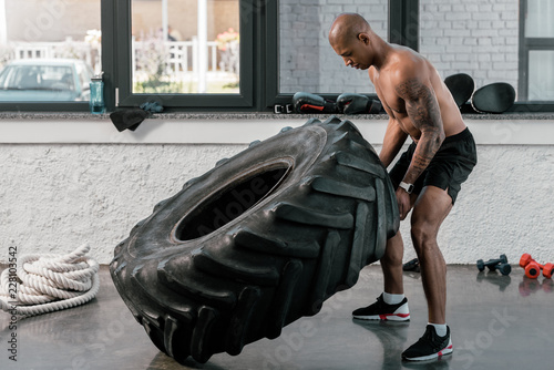 muscular shirtless young african american man exercising with tyre in gym