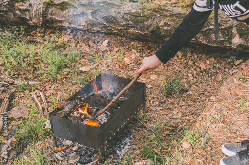 Tourist with a stick moves the coal in the brazier in the woods