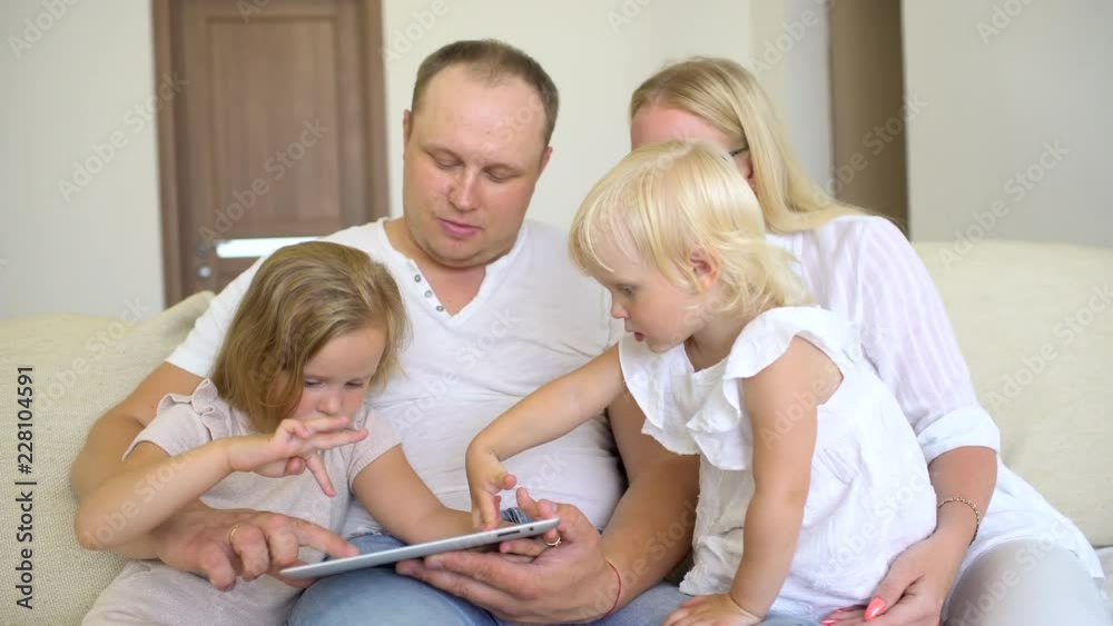 Happy family playing together with laptop and digital tablet at home. Father, mother and two kids sitting on sofa and using tablet computer, watching video, film in room. Happiness. 4 K Happy family playing together with laptop and digital tablet at home. Father, mother and two kids sitting on sofa and using tablet computer, watching video, film in room. Happiness. 4 K