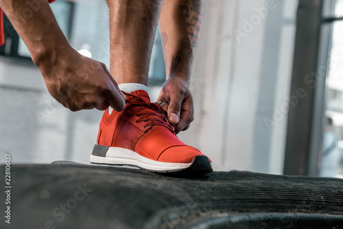 cropped image of sportsman tying laces of red sneakers at gym photo