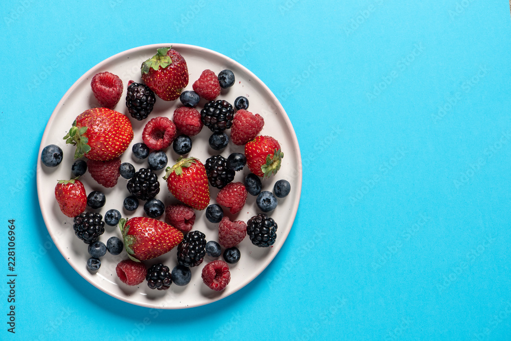 Top view of a plate with variety of forest fruits, berries on a blue background Top view of a plate with variety of forest fruits, berries on a blue background