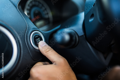 Finger of man press start button engine of car with black color interior of car