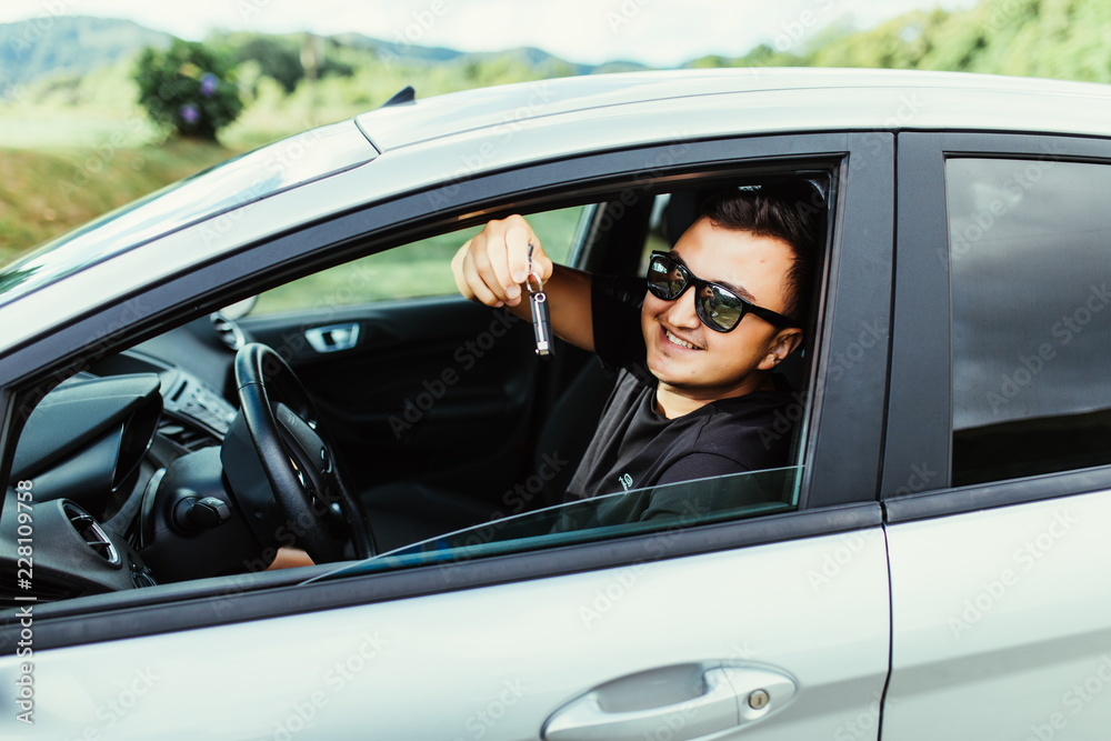 Young man in sunglasses sitting in car holding car keys outdoors