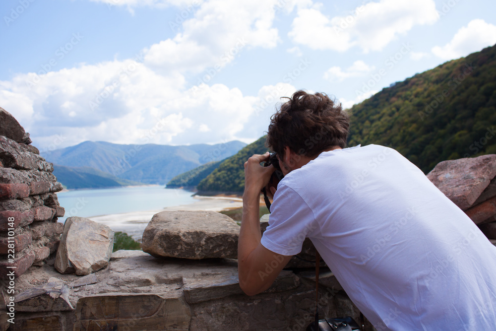 Naklejka premium Young curly traveler taking photo with camera in Ananuri Castle