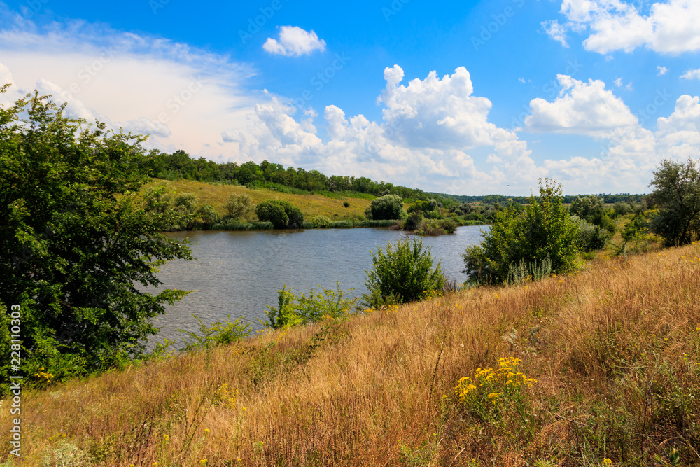 Summer landscape with beautiful lake, green meadows, hills, trees and blue sky Summer landscape with beautiful lake, green meadows, hills, trees and blue sky