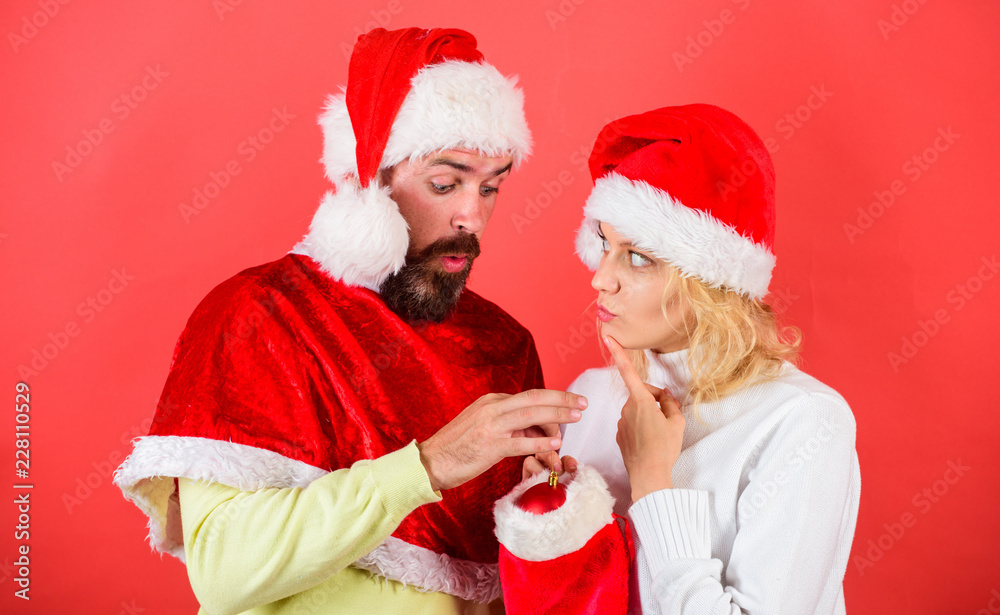 Obraz premium Woman and bearded man in santa hat expecting gift red background. Check contents of christmas stocking gift received. Christmas gift concept. Couple cheerful face check out gift in christmas sock