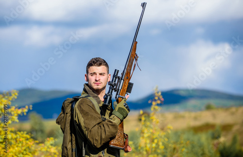 Man brutal guy gamekeeper nature background. Hunter rifle gun stand top of mountain. Guy bearded hunter spend leisure hunting on birds. Hunting masculine hobby concept. Regulation of hunting