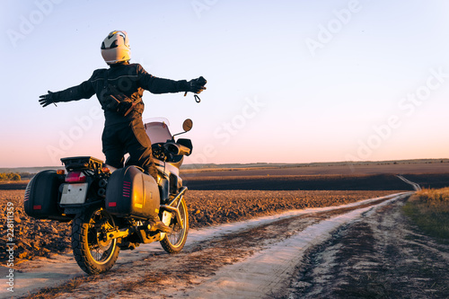 Motorbiker travelling, autumn day, motorcycle off road, the driver stands with open arms to the side, to meet a new day, adventurer, extreme tourism, cold weather clothes