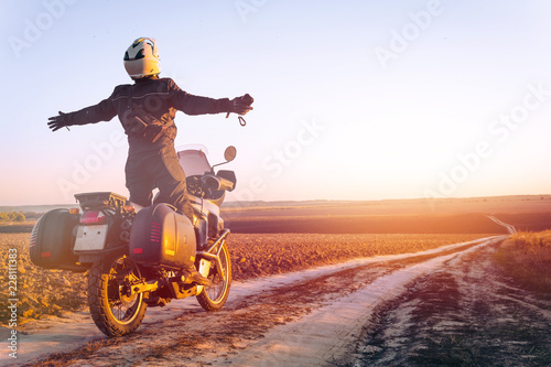 Motorbiker travelling, autumn day, motorcycle off road, the driver stands with open arms to the side, to meet a new day, adventurer, extreme tourism, cold weather clothes, light tinting