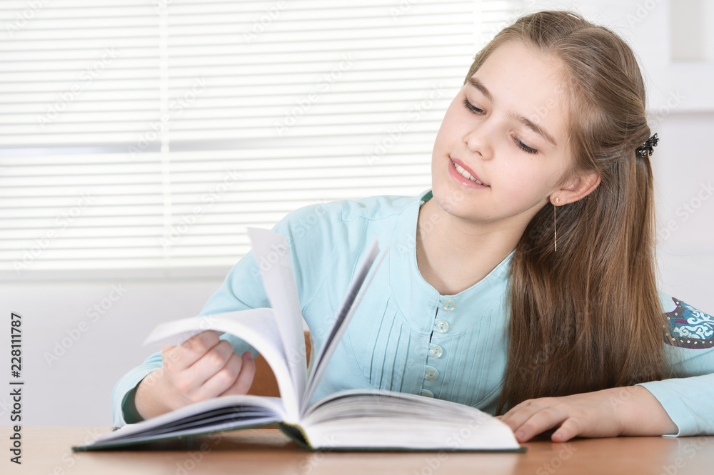 Cute schoolgirl sitting at table and reading Cute schoolgirl sitting at table and reading