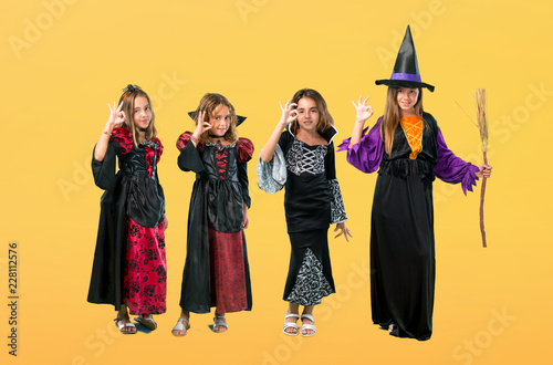 Set of Little girl dressed as a vampire for halloween holidays showing an ok sign with fingers on orange background