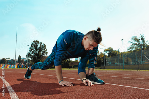 The fit male runner stretching legs preparing for run during training at stadium tracks. The athlete, fitness, workout, sport, exercise, training, athletic, lifestyle concept