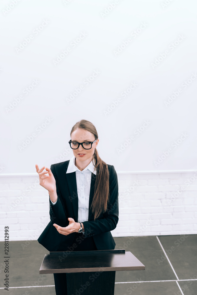 high angle view of attractive lecturer standing and gesturing at podium tribune during seminar in conference hall high angle view of attractive lecturer standing and gesturing at podium tribune during seminar in conference hall