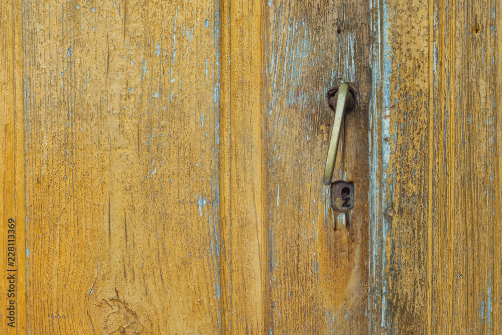 Wooden surface with old yellow paint and a door handle. Close-up. Background. Texture Wooden surface with old yellow paint and a door handle. Close-up. Background. Texture