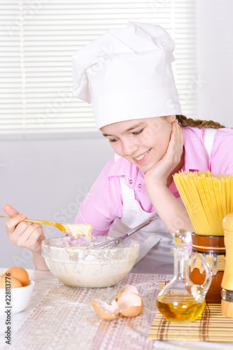 Cute girl in chef's hat cooking in the kitchen