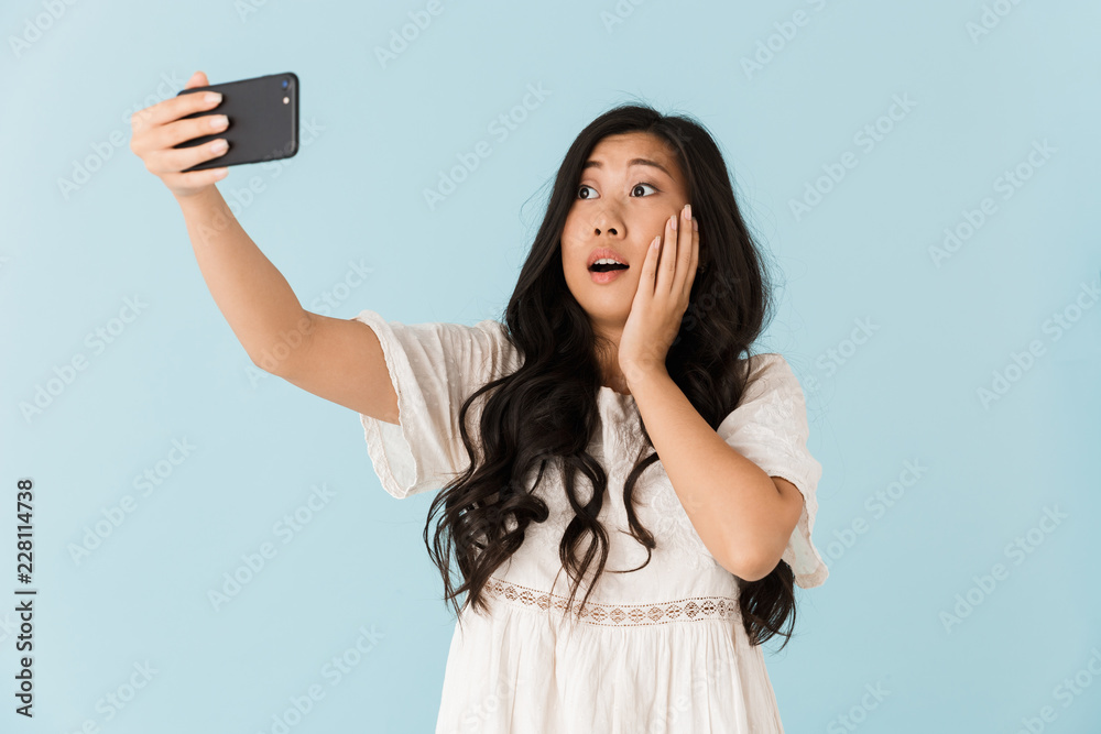 Beautiful woman isolated over blue background take a selfie by mobile phone. Beautiful woman isolated over blue background take a selfie by mobile phone.