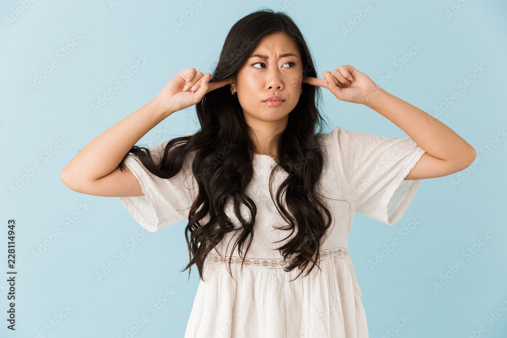 Displeased young asian beautiful woman isolated over blue background covering ears.
