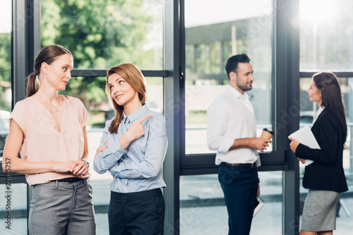 businesswomen gossiping while collegaues having conversation behind in office photo